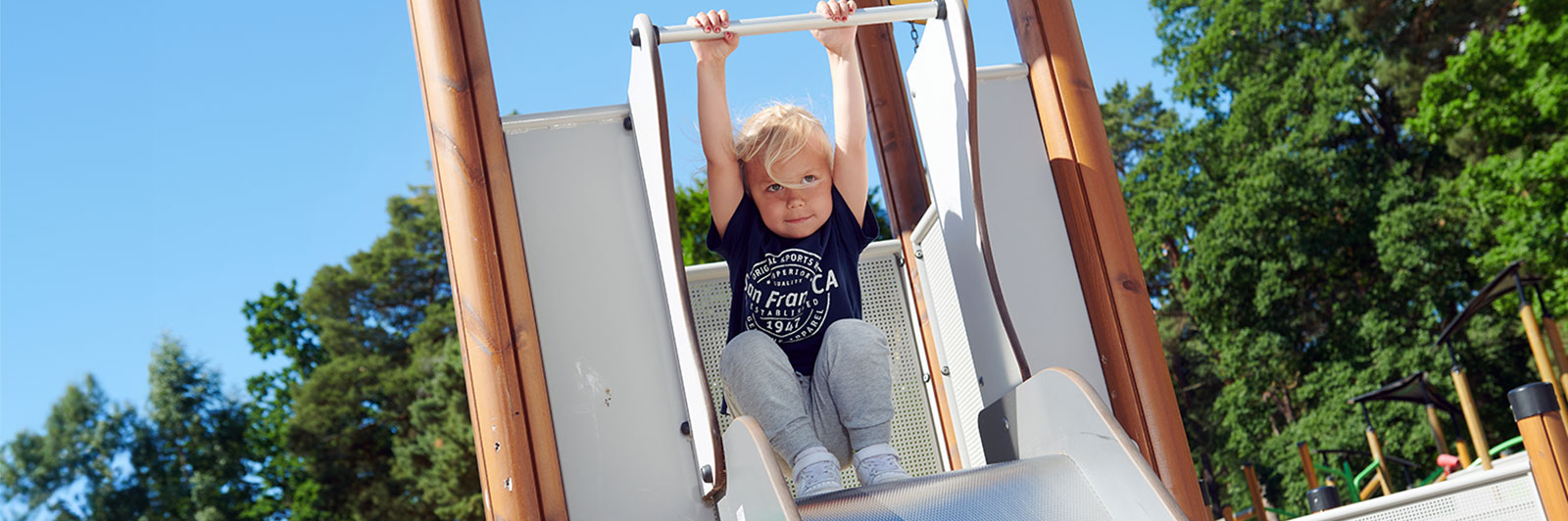 A young boy is holding onto the railing at the top of a slide, ready to slide down at a playground.